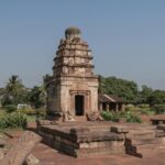 Ancient stone temple surrounded by lush greenery in Aihole, Karnataka, India.