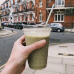 Hand holding a green smoothie in a disposable cup on a street in Greater London, UK.