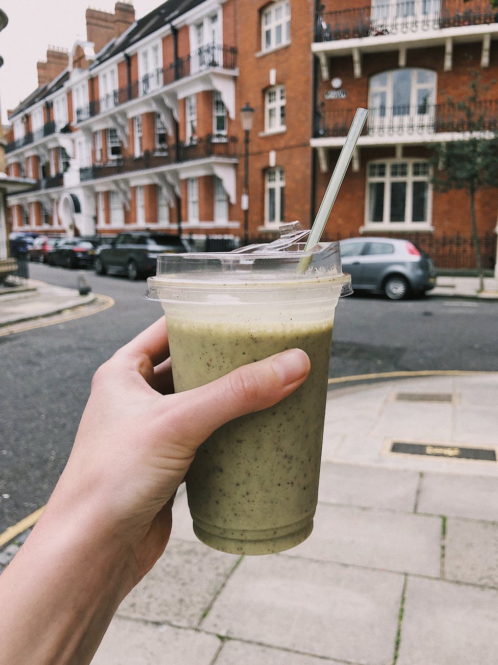 Hand holding a green smoothie in a disposable cup on a street in Greater London, UK.