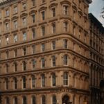 A historic hotel with classic architecture, featuring two people walking by on a city street during dusk.