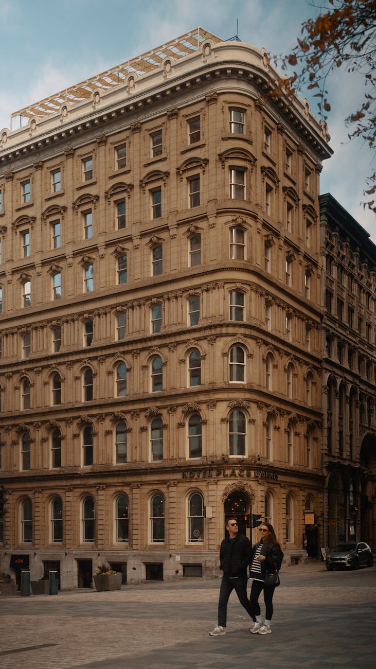 A historic hotel with classic architecture, featuring two people walking by on a city street during dusk.