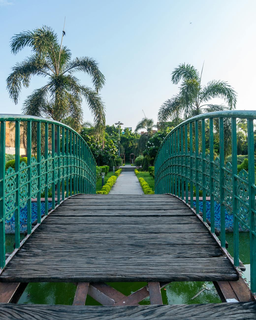 A picturesque footbridge spans lush gardens, framed by palm trees in a serene park.
